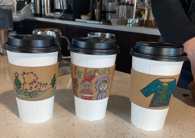 Winning designs of hot cup sleeves chosen by owner Ann Shultz at La Petit Bistro, designed by Aria, Matteo and Ben- young artists at the Woodburn Art Center.